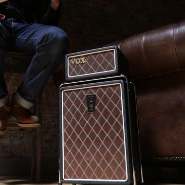 partial view of man sitting on stool playing guitar beside VOX amplifier